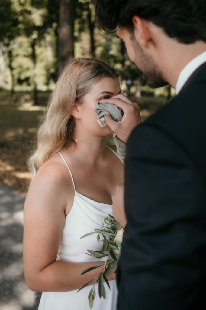 Mit einem grünen Stofftuch trocknet der Bräutigam eine Träne der Braut.