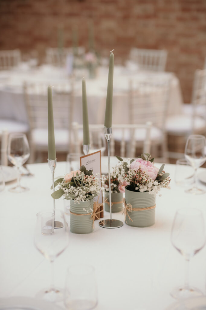 Diese Nahaufnahme zeigt die in mintgrün-rosa gehaltene Tischdekoration aus schmalen Kerzen und niedrigen Blumentöpfchen.