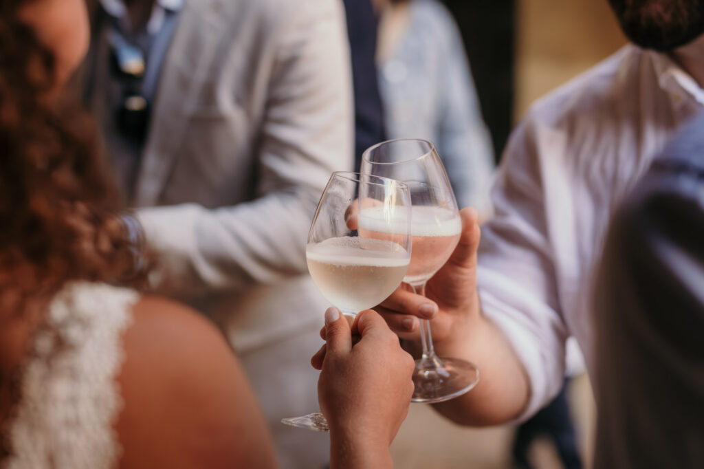 In einer Nahaufnahme sieht man wie die Braut mit einem männlichen Gast mit Weißwein anstößt.