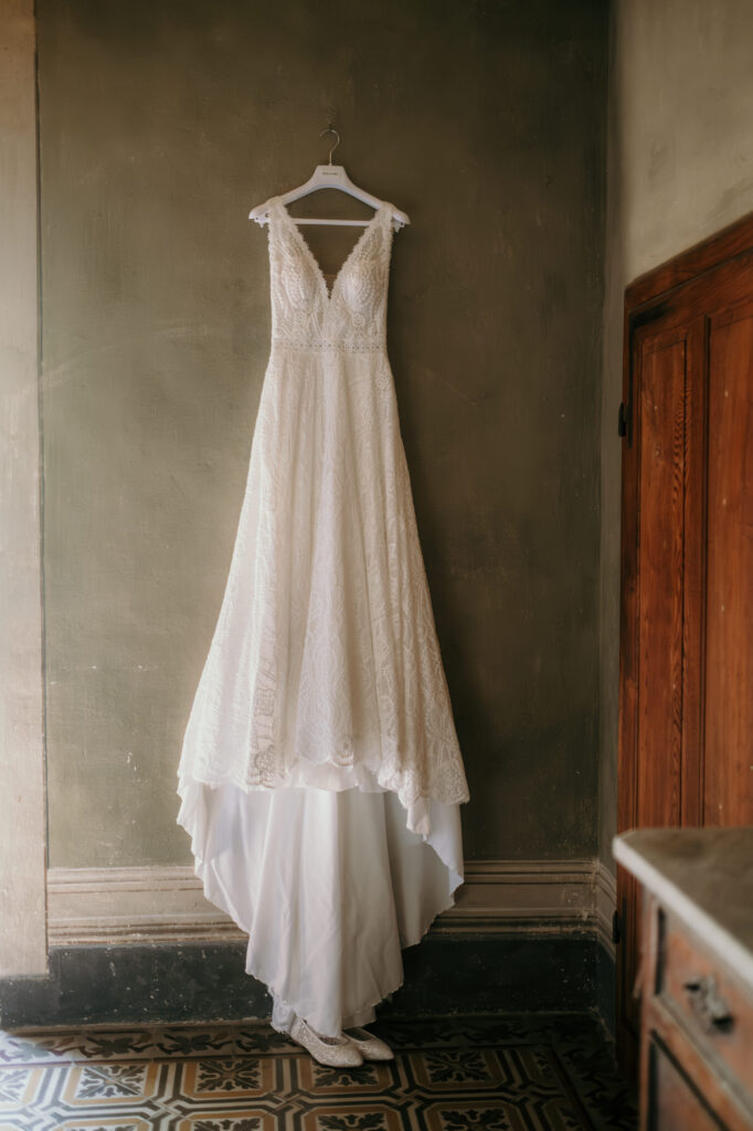 Das Hochzeitskleid der Braut hängt auf einem weißen Kleiderbügel an einer Wand bereit.