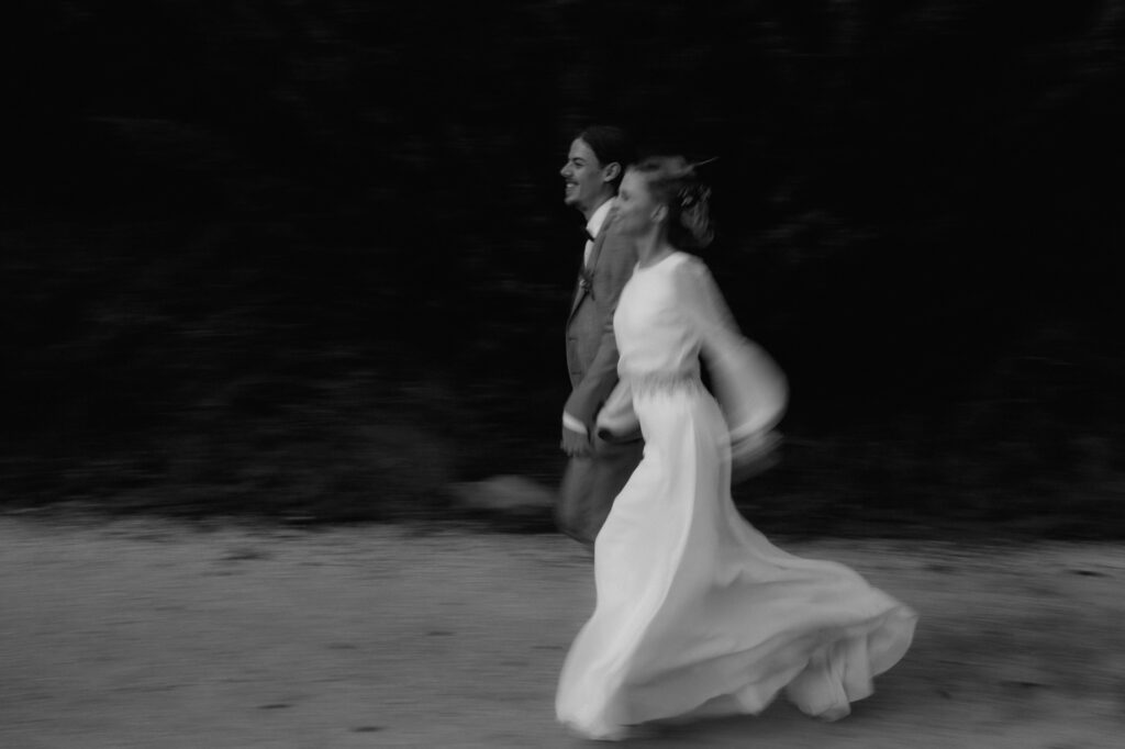 Das Hochzeitspaar rennt seitlich betrachtet lächelnd einen Weg entlang.