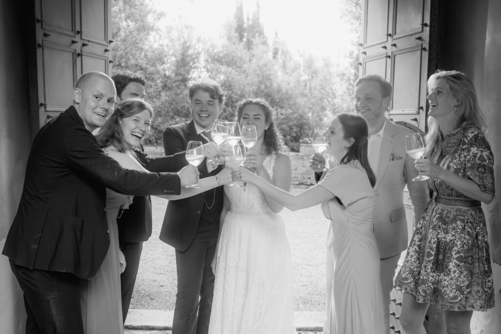 In gelöster Stimmung stoßen Hochzeitspaar und sechs ihrer Gäste fröhlich an.