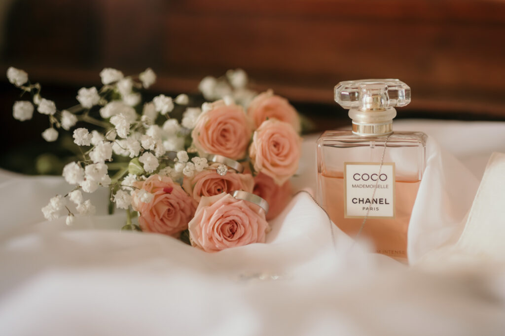 Ein kleiner Strauß aus rosafarbenen Rosen und Schleierkraut liegt neben dem Parfüm der Braut.