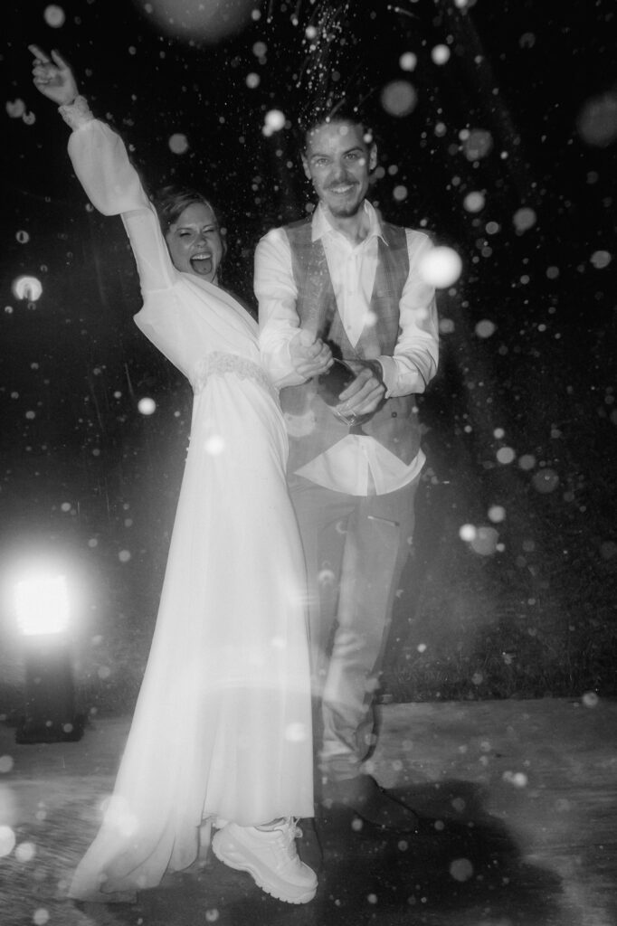 Die Braut reckt vor Euphorie ihren Arm nach oben, während der Bräutigam den Champagner verspritzt.