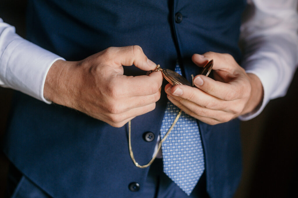 Seine dunkelblaue Weste tragend wirft der Bräutigam einen Blick auf seine goldene Taschenuhr.