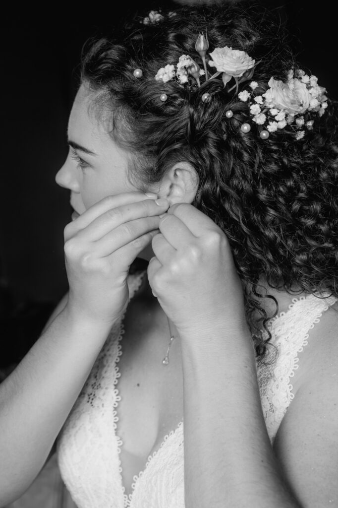 Fertig frisiert steckt sich die Braut ihre Ohrringe an.