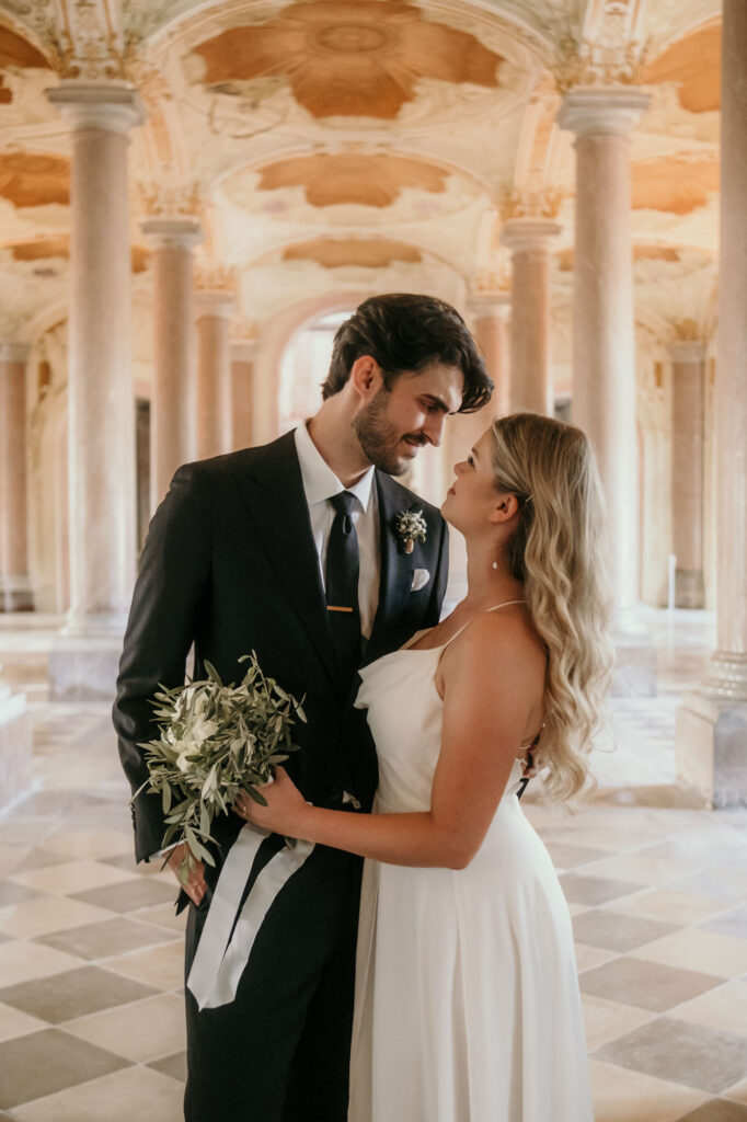 Verliebt sieht sich das Hochzeitpaar in die Augen, während es in der hohen Säulenhalle steht.
