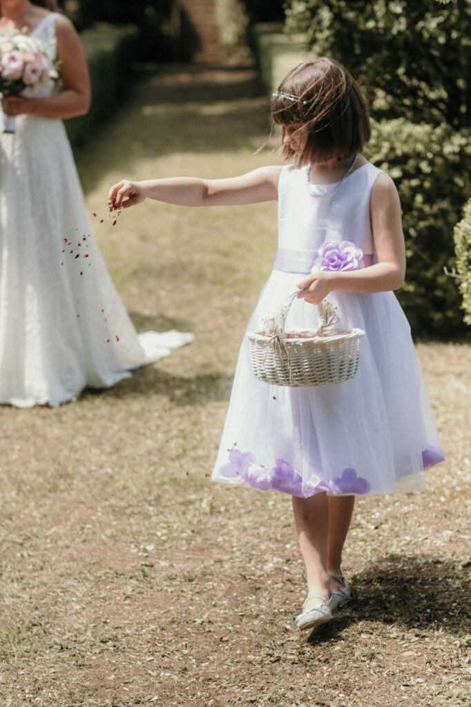 Ein Blumenmädchen mit einem weißen Kleidchen streut für den Einzug der Braut Blüten.