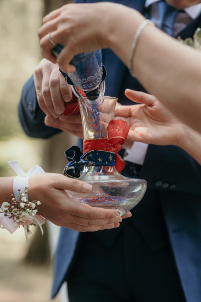 Das Hochzeitspaar befüllt bei einem Ritual eine Glaskaraffe mit je roten und blauen Steinchen.