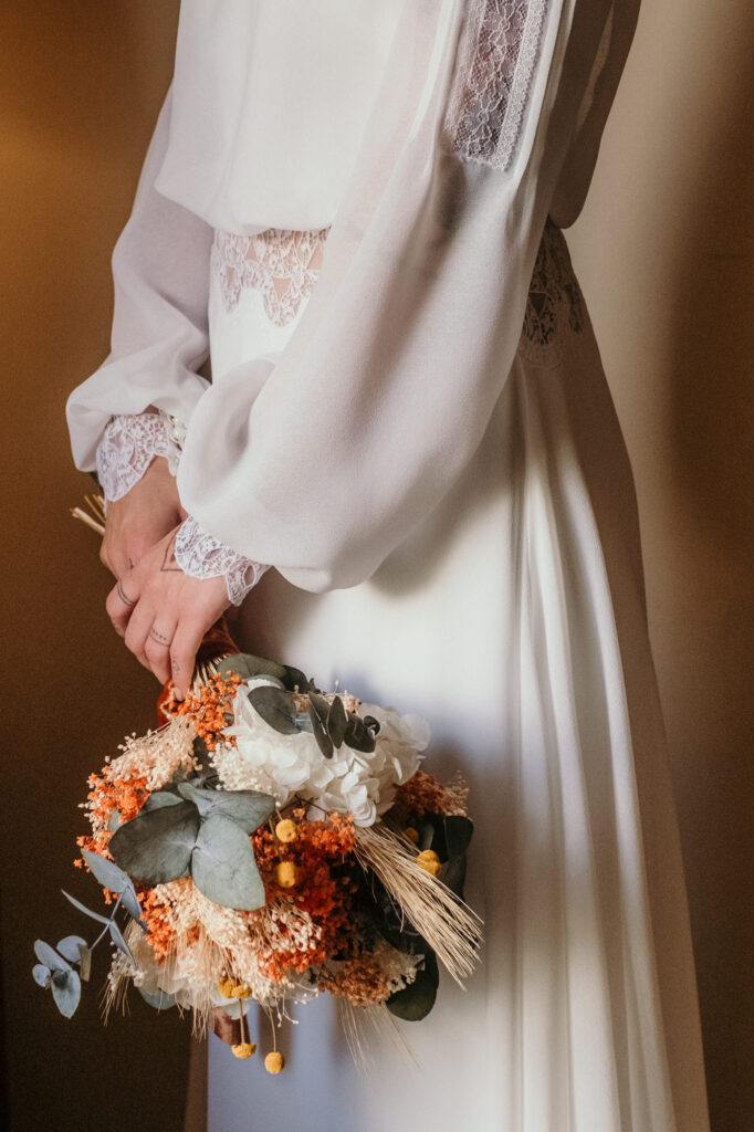 Seitlich stehend hält die fertig gestylte Braut ihren Brautstrauß locker mit beiden Händen.