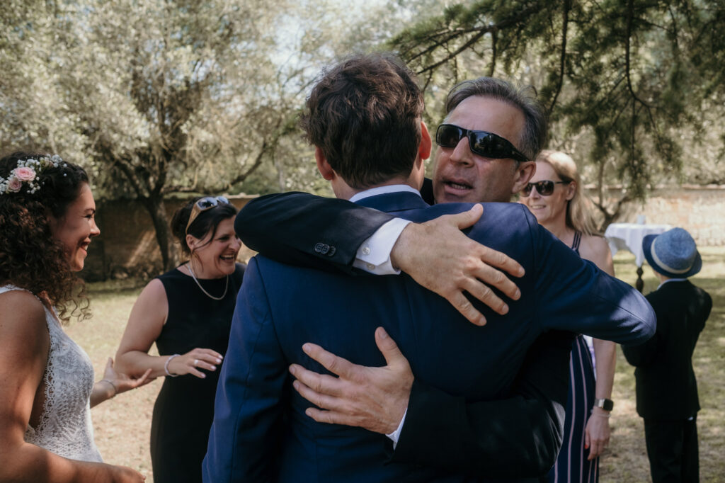 Der Bräutigam wird bei den Gratulationen von einem Herren mit schwarzer Sonnenbrille umarmt.