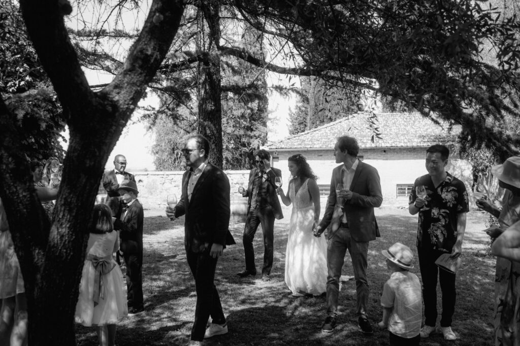 Einige Gäste und das Brautpaar laufen mit Gläsern in der Hand in Richtung eines Baums.