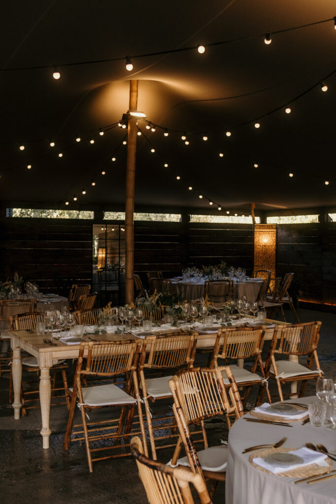 Ein Blick in den Hochzeitssaal zeigt gedeckte Holztische mit Bambusstühlen, darüber hängt eine Lichterkette.