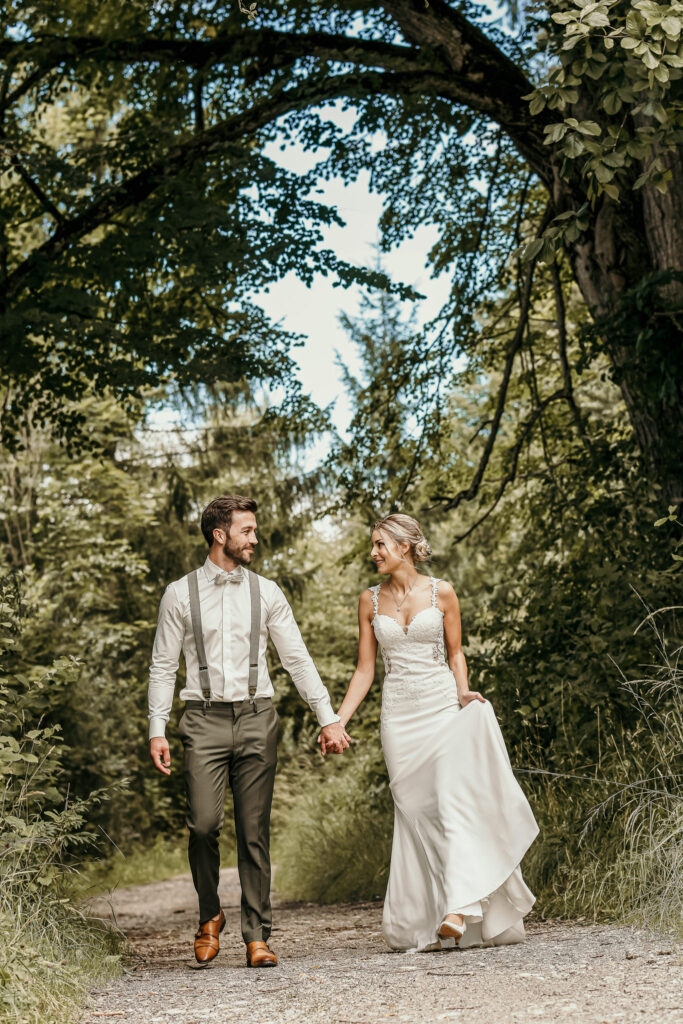 Das Hochzeitspaar spaziert sich anblickend über einen Feldweg, gesäumt von Bäumen.
