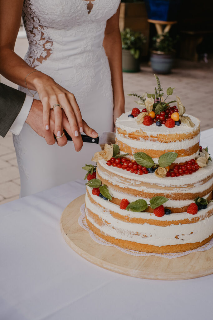 Das Hochzeitspaar schneidet ihre Hochzeitstorte - einen mit Obst bestückten Naked Cake - an.