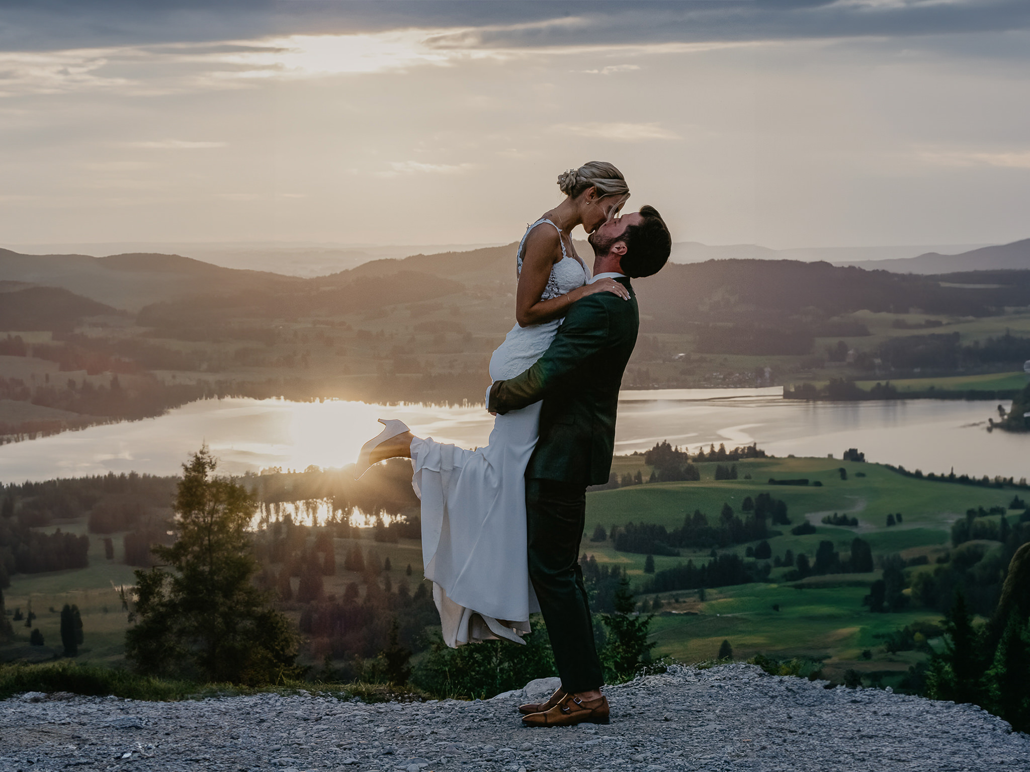 Vor dem Sonnenuntergang der alpinen Landschaft hebt der Bräutigam seine Braut für einen Kuss hoch.
