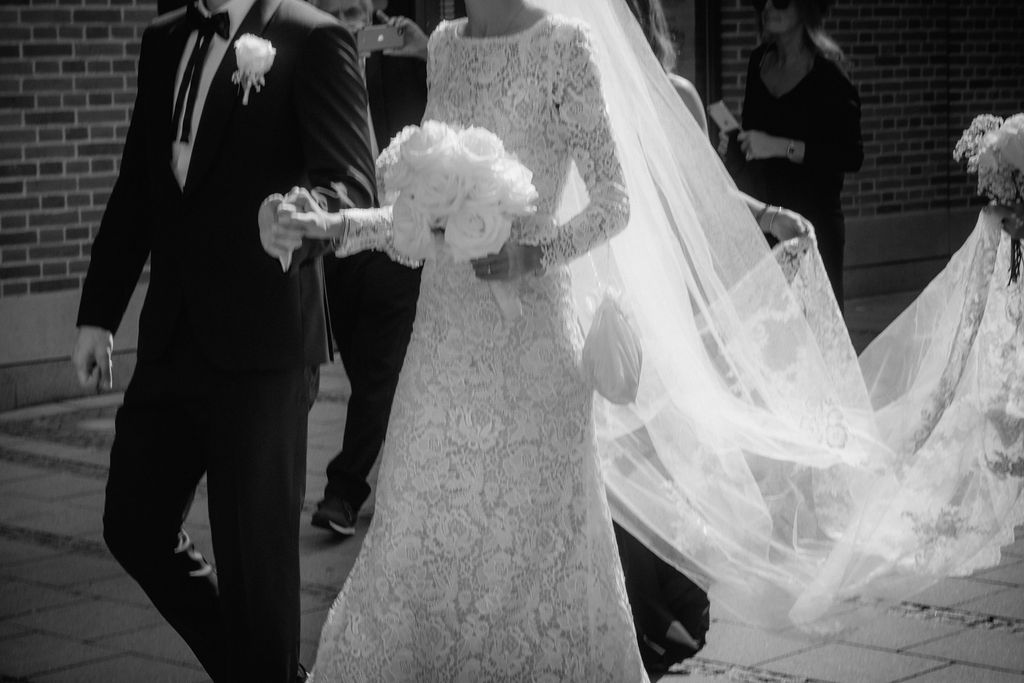 Ein schwarz-weiß Bild von einem Paar in ihren Hochzeitsoutfits, das Hand in Hand durch die Innenstadt geht.