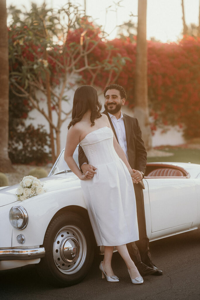 A couple leaning on their wedding car in the morning light